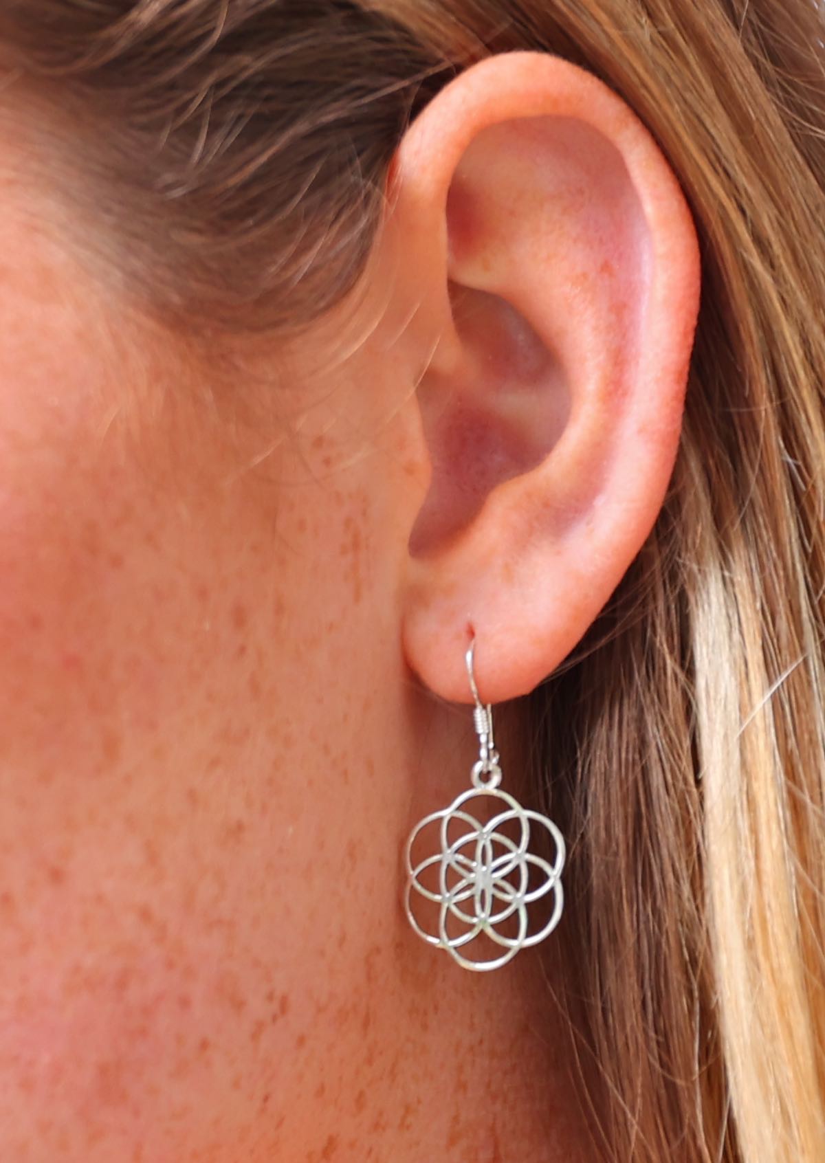 Close up of sterling silver earring with seven circles, intersecting each other, suspended from a wire hook