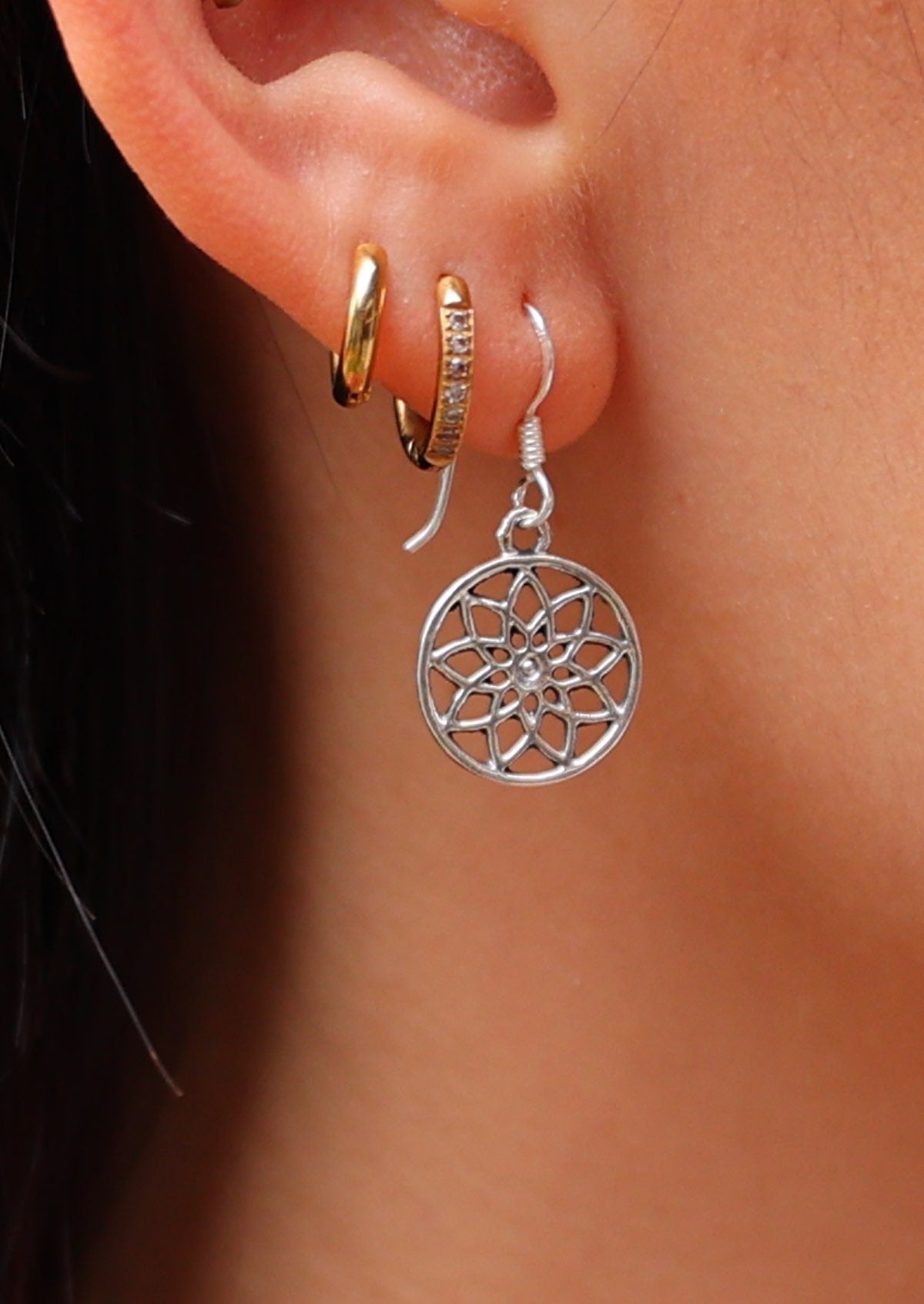 Close up of silver sacred flower earring suspended from wire hook