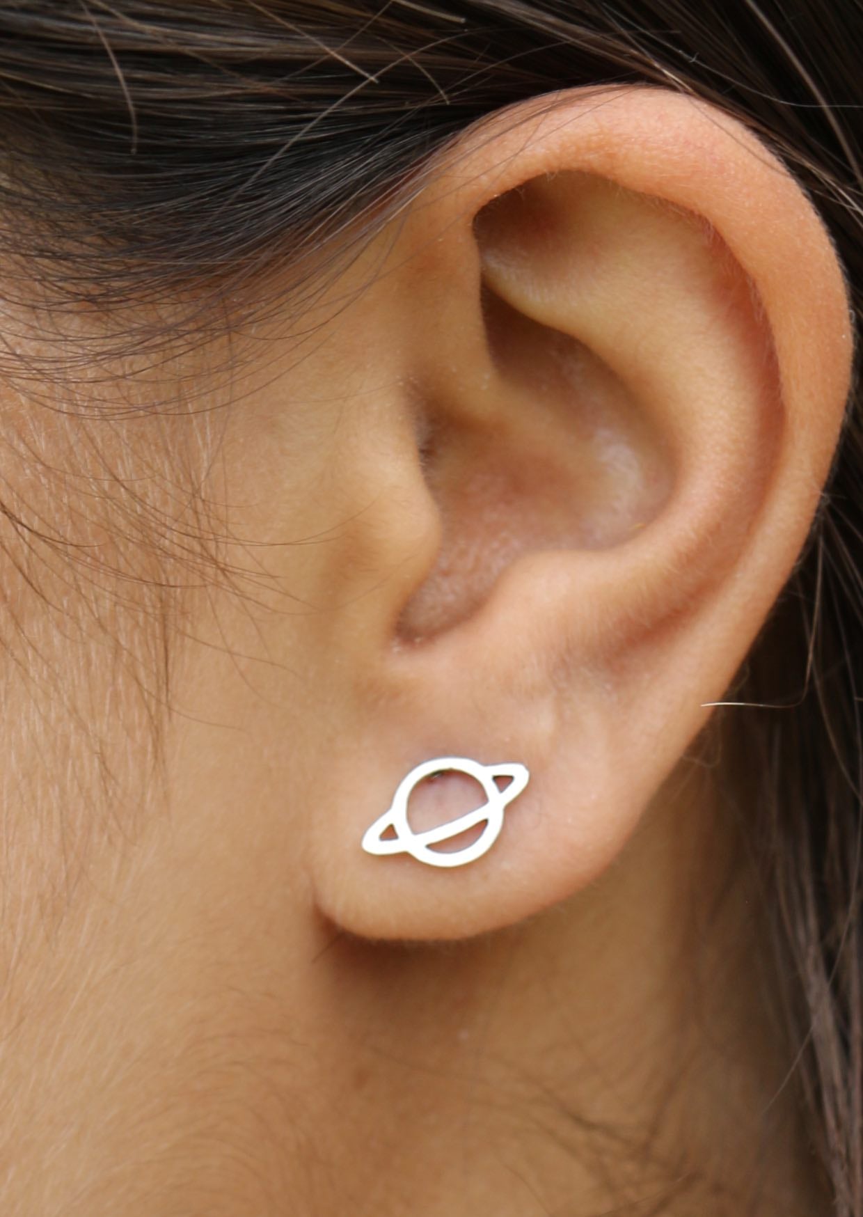 Close up of a person wearing a sterling silver saturn cutout studs with butterfly backs