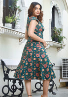 Model standing on side wearing green 100% cotton scoop neck retro dress with fuller skirt and cap sleeves.