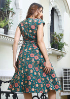 Model standing on back wearing a knee length, floral print cotton dress with zip at the center of the back