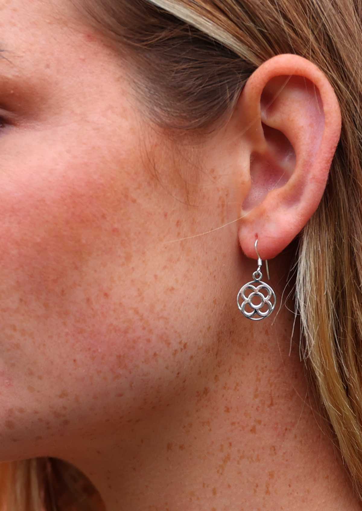 Close up of silver earring with stylised four petal flower cutout