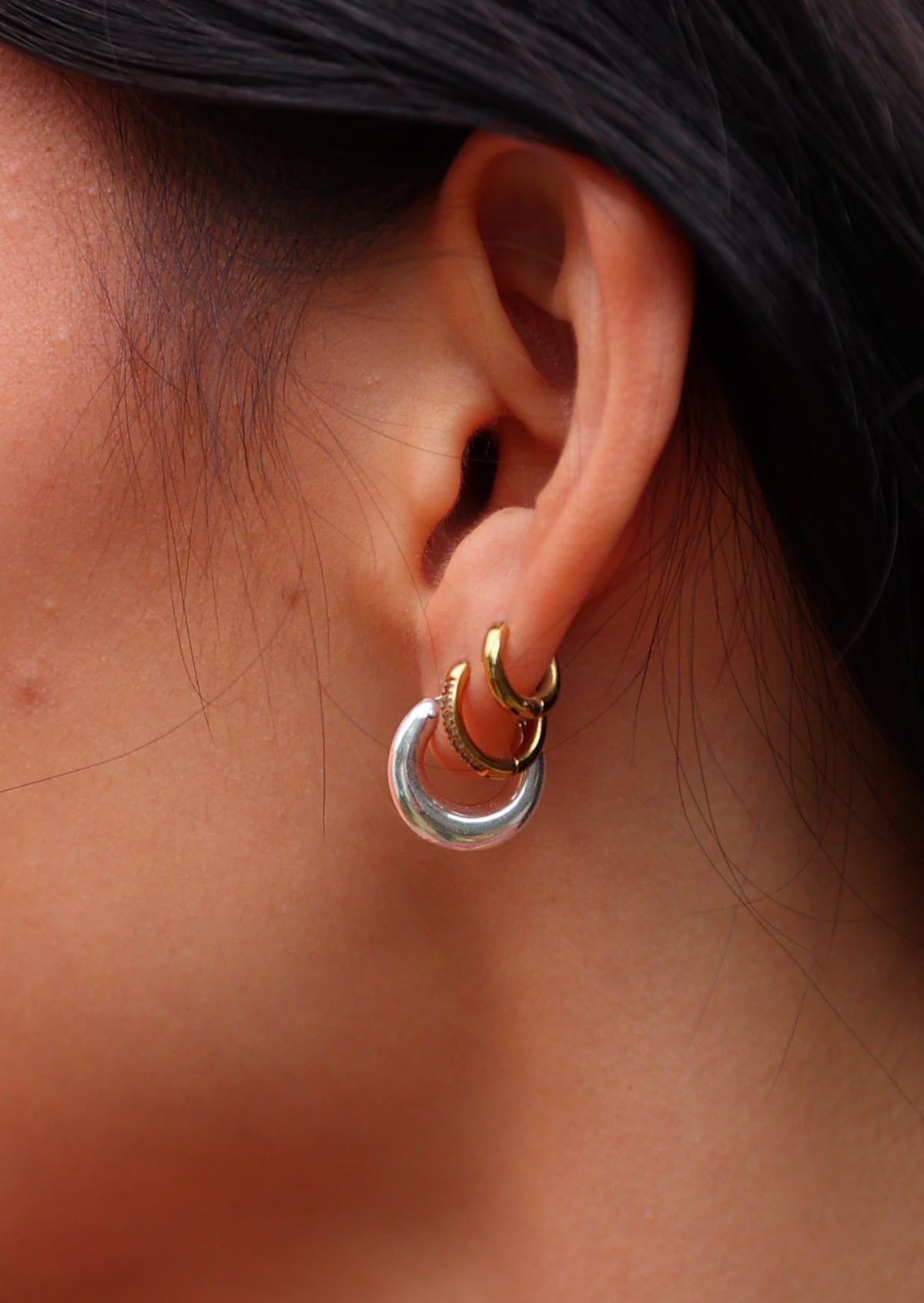 Close up of model wearing small chunky sterling silver hoop earring with her own small gold hoops