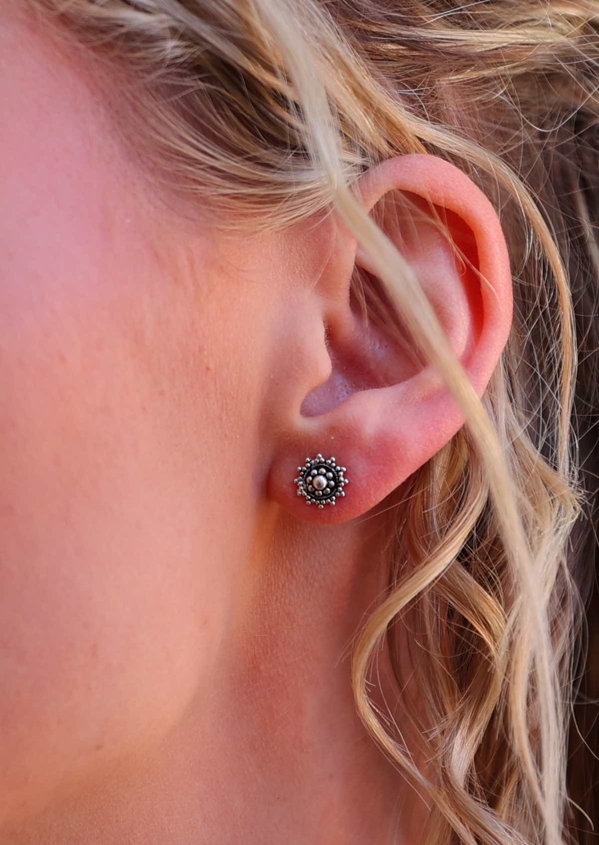 Close up of Silver Ornate stud earrings with intricate designs, displayed in woman's ear