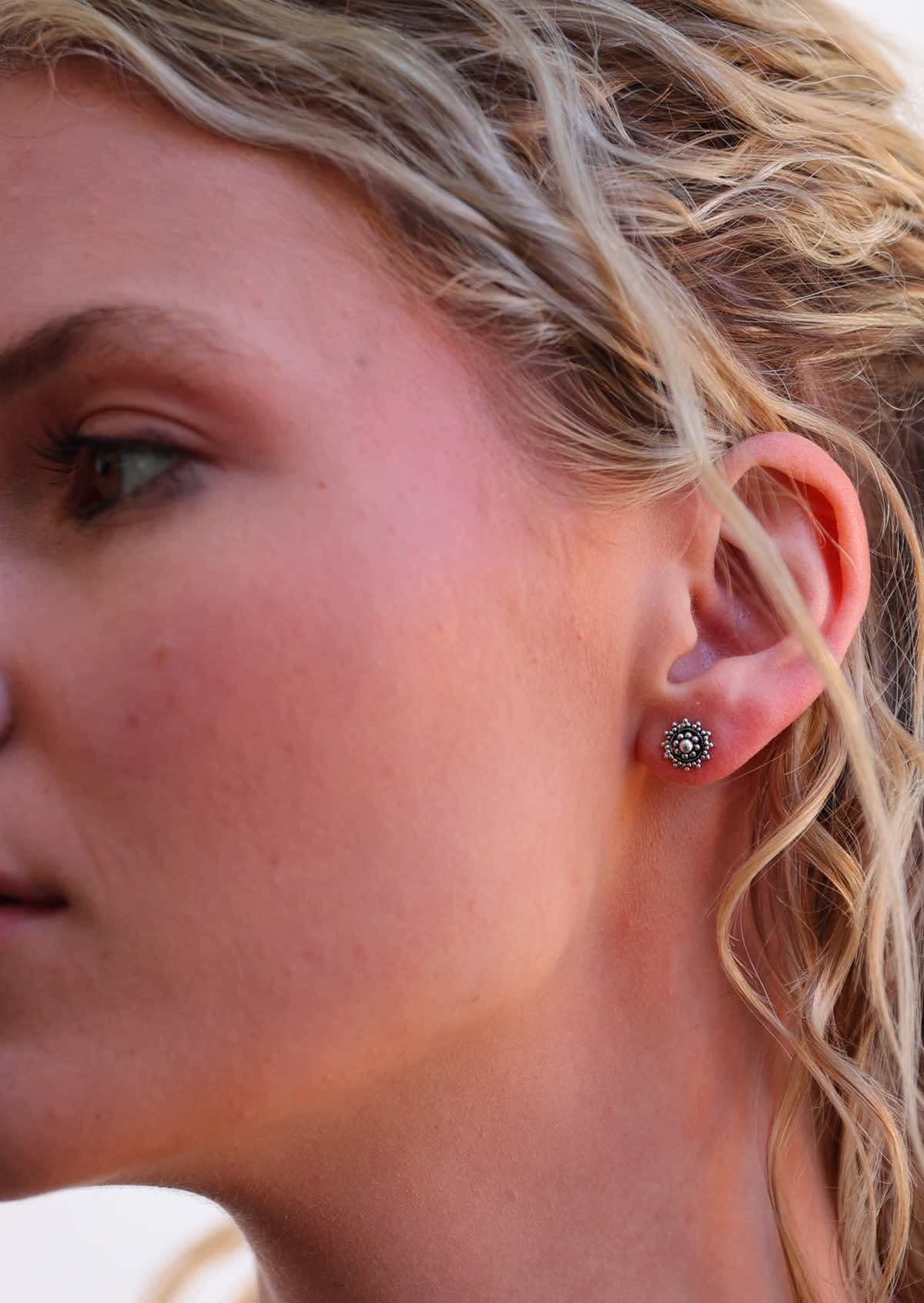 Silver Ornate stud earrings with intricate designs, displayed in woman's ear