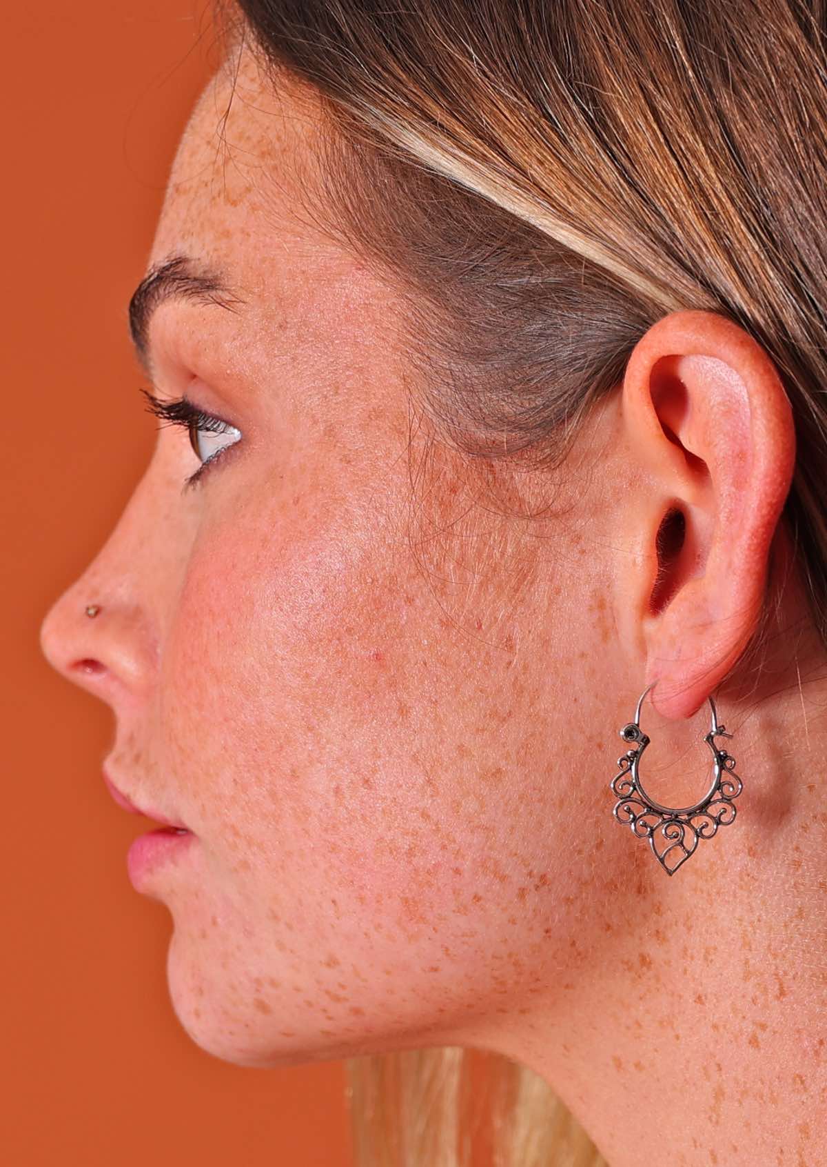 Woman wears sterling silver hoop earrings with small spiral details on the underside of the hoop