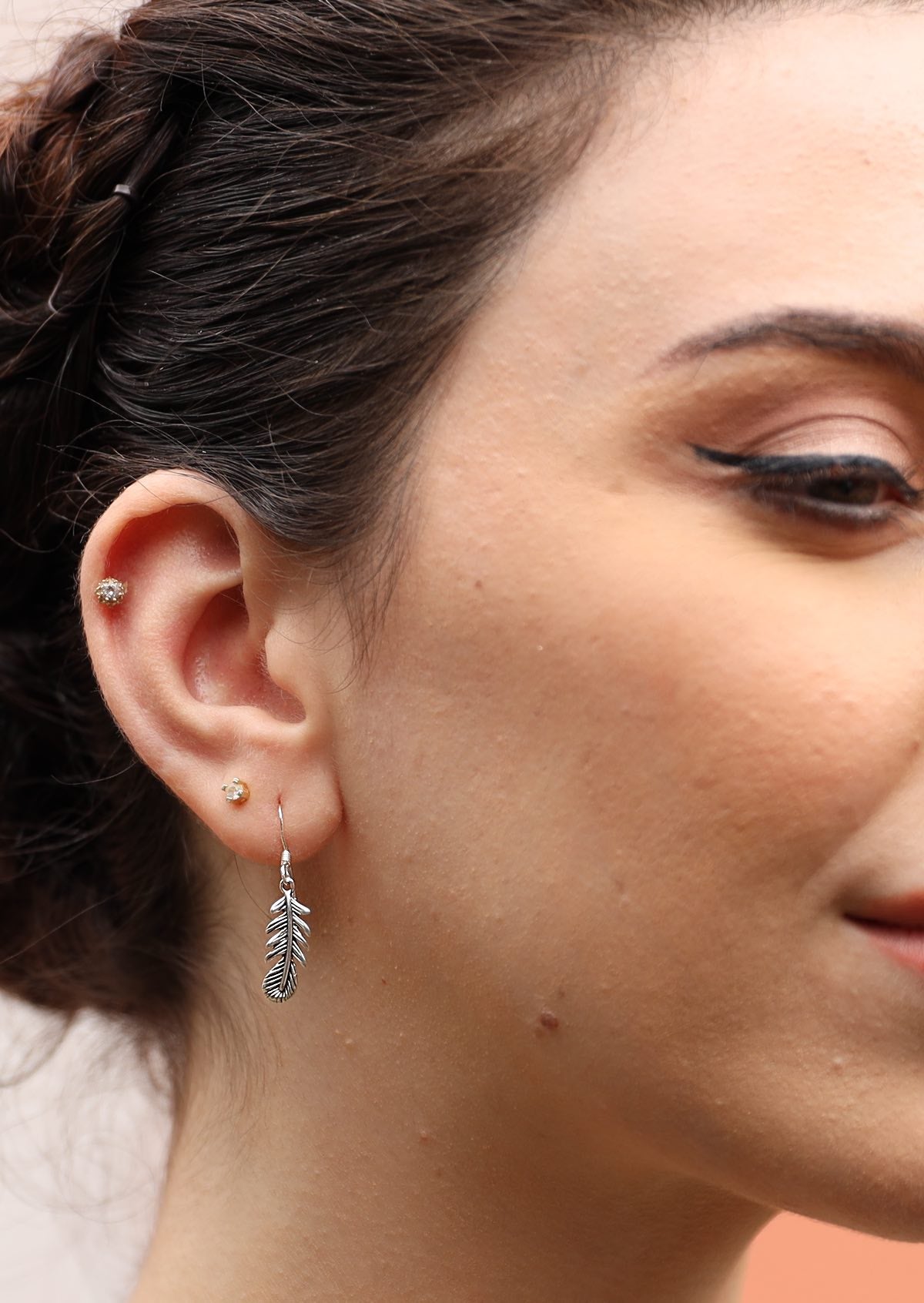 Woman wears silver feather earring, approx 32mm long, including wire hook