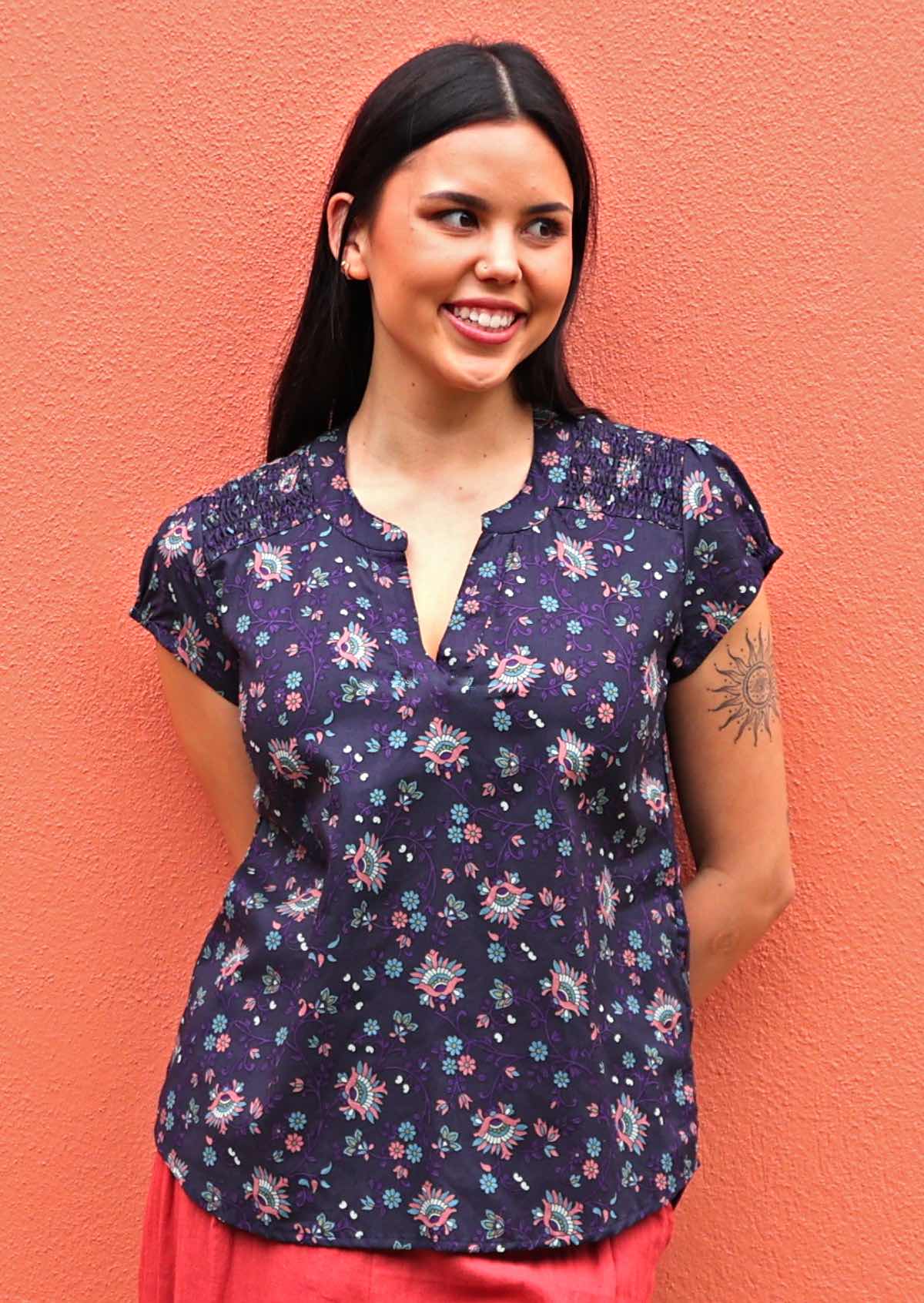Model wearing capped sleeve cotton blouse in an Indian floral print standing against coral coloured wall