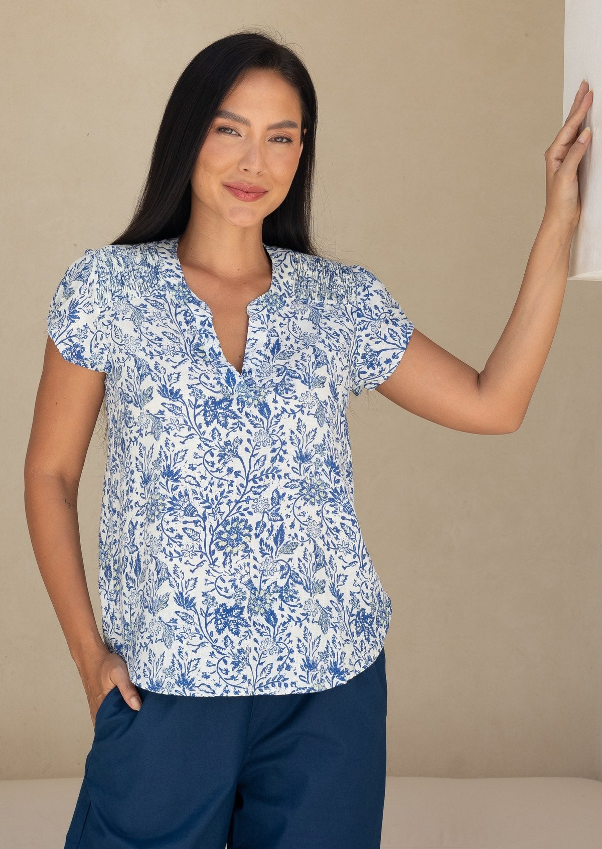 woman wearing a white based blue floral print cotton top against a white background.