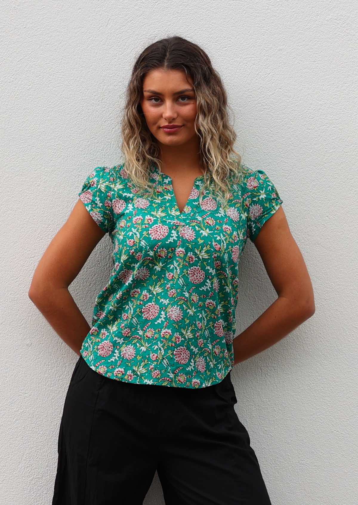 Model poses in cotton cap sleeve top with a V-neckline and mandarin collar, in floral print on a jade green base