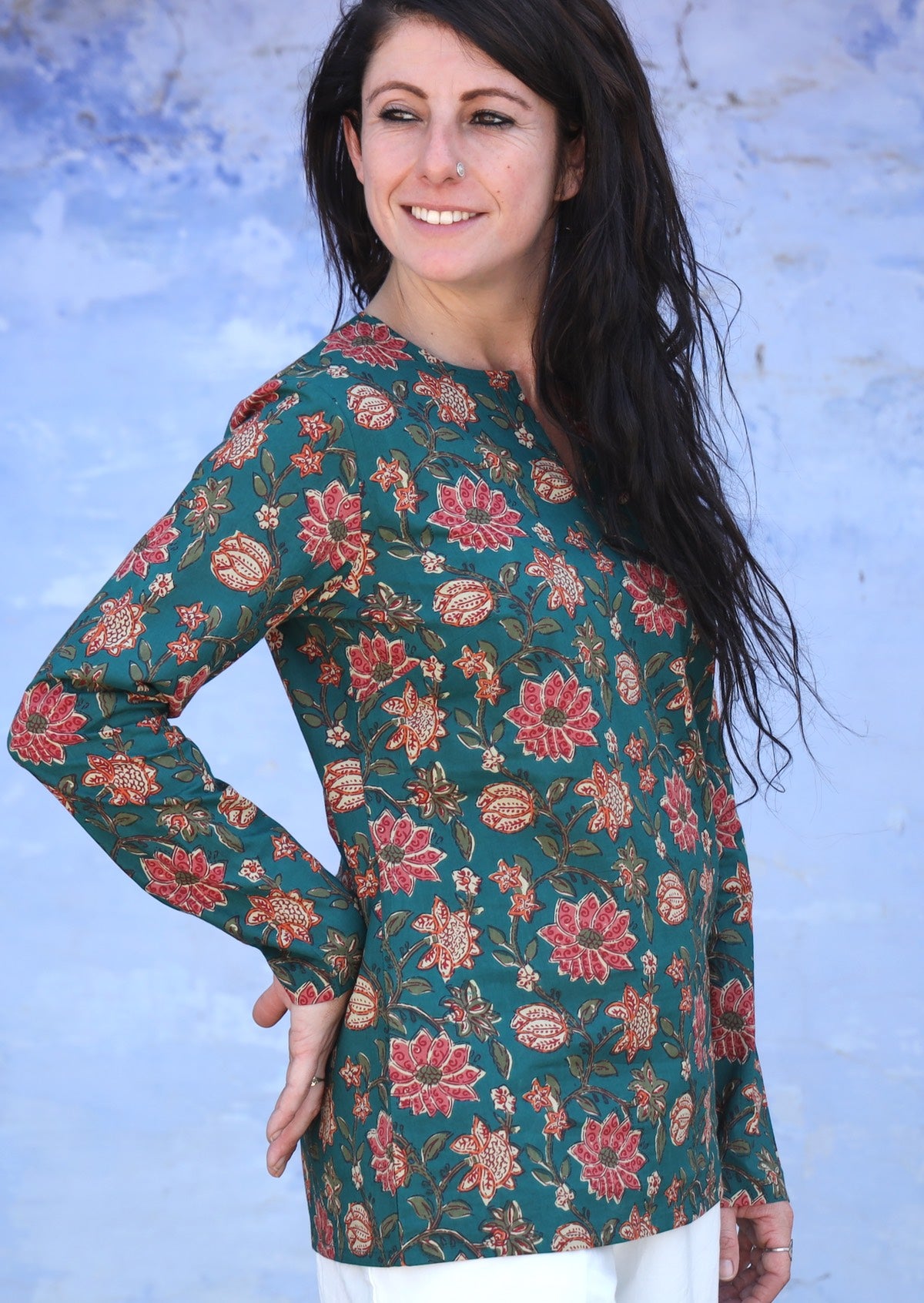 Model poses side on in long sleeve cotton top in floral print on a green base