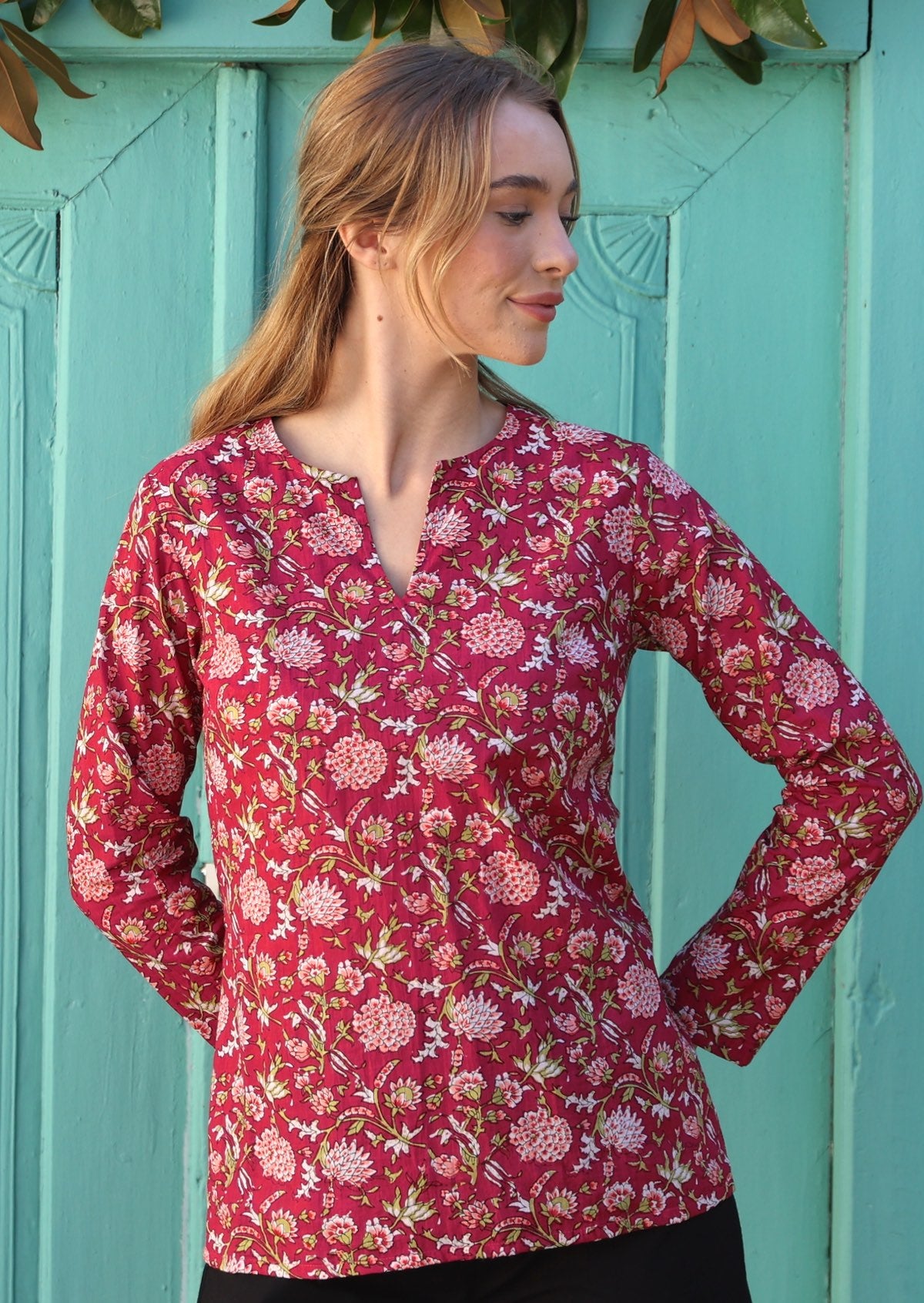 Model standing near aqua door wears lightweight cotton top in beautiful red and pink floral print.
