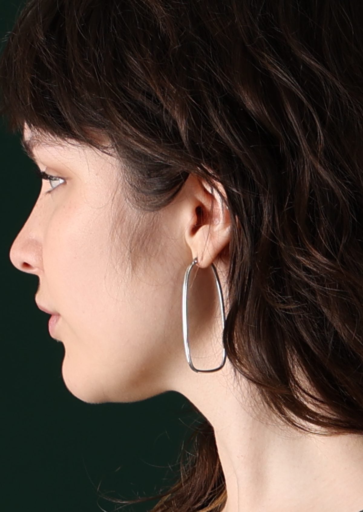 Model with dark hair wearing elongated large silver hoop earrings