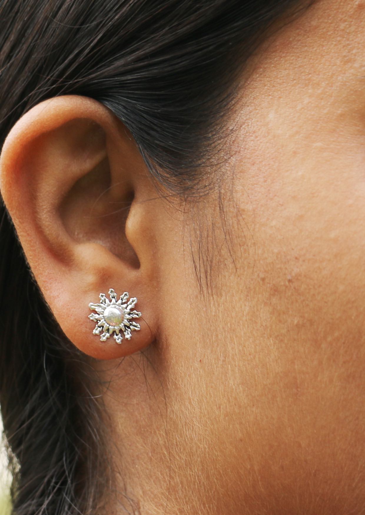 Close-up of an ear wearing a delicate silver sun blossom studs with intricate detailing