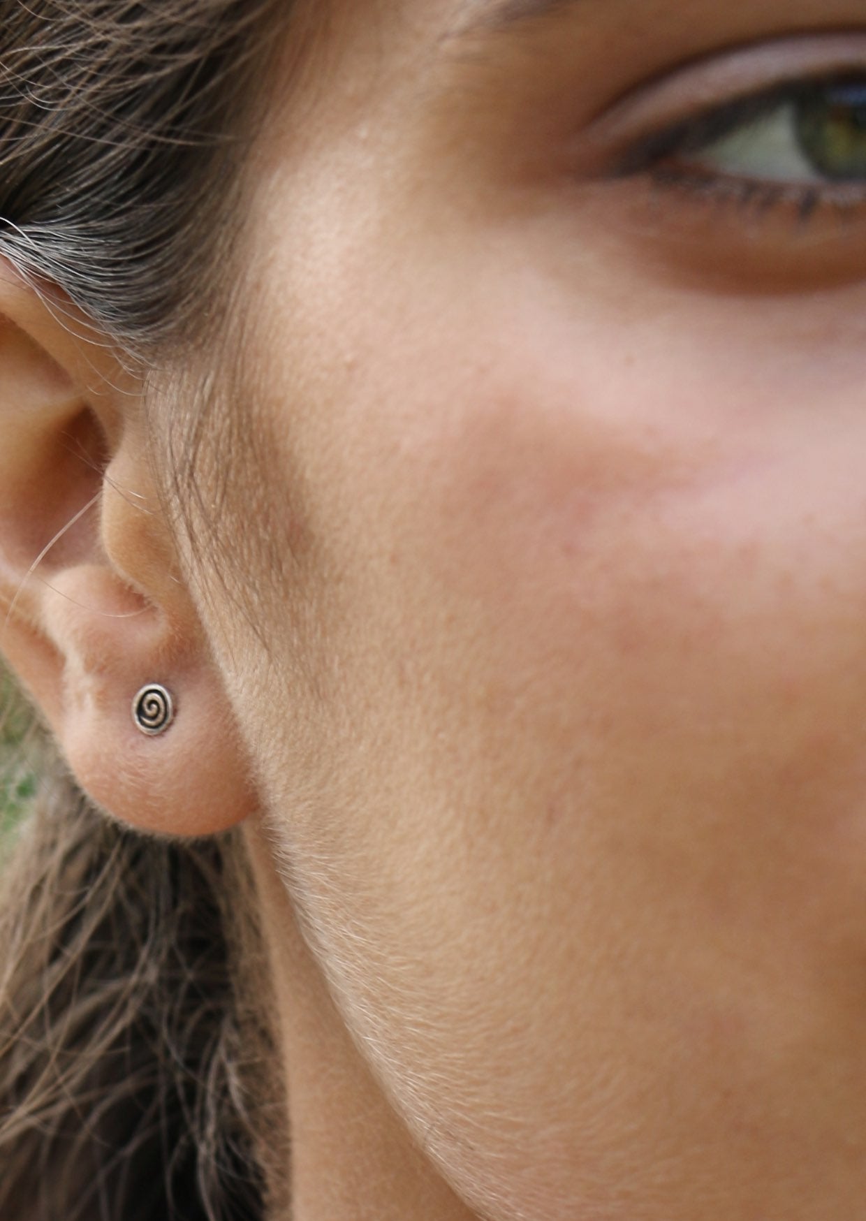 Close-up of a person's ear with a small sterling silver swirls studs with a disk having a delicate swirl design on the front