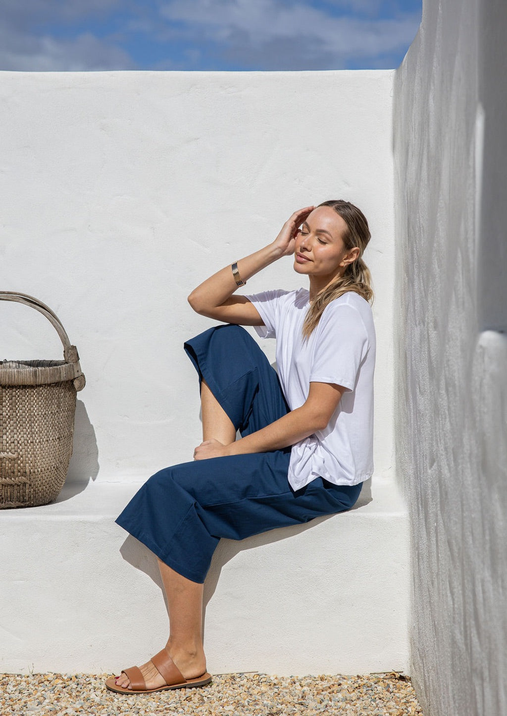 Model is sitting in dark blue 3/4 length wide-leg cotton pants with a wide waistband, side zipper, and pockets