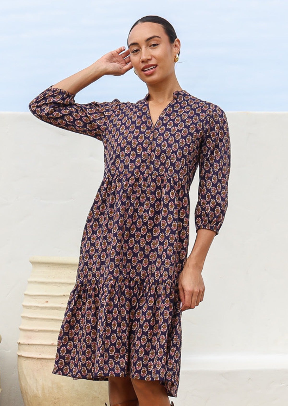 Model poses in cotton tiered dress with a buttoned bodice and mandarin collar and 3/4 sleeves
