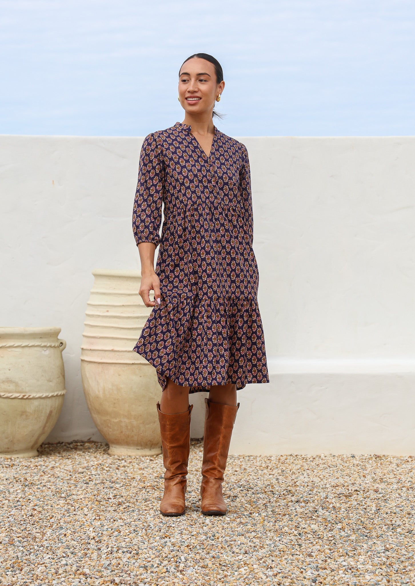 Model wears over the knee length cotton relaxed fit dress with buttoned bodice, V-neckline and mandarin collar