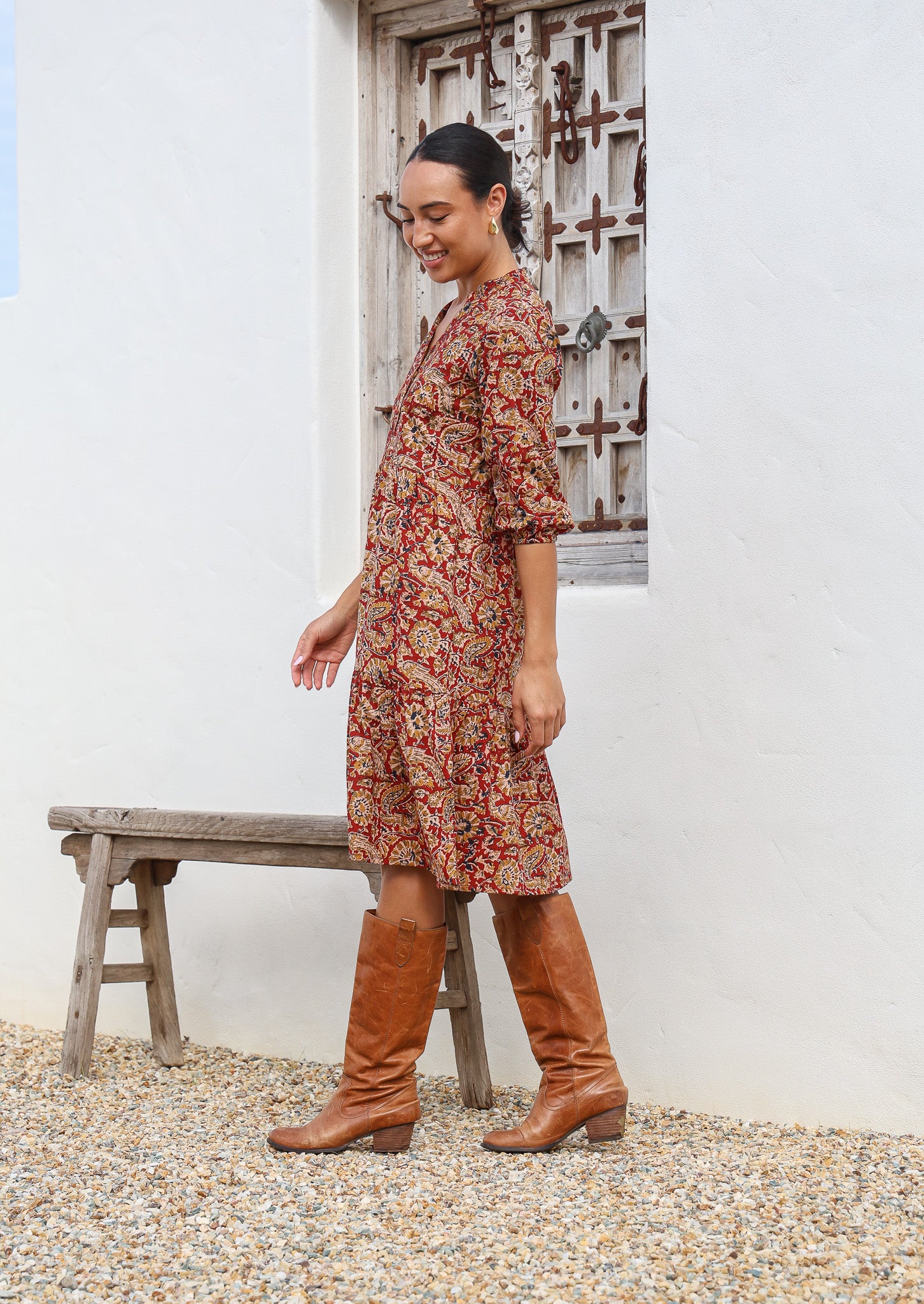 Model stands side on in cotton over the knee length relaxed fit dress with 3/4 sleeves, paired with tan boots