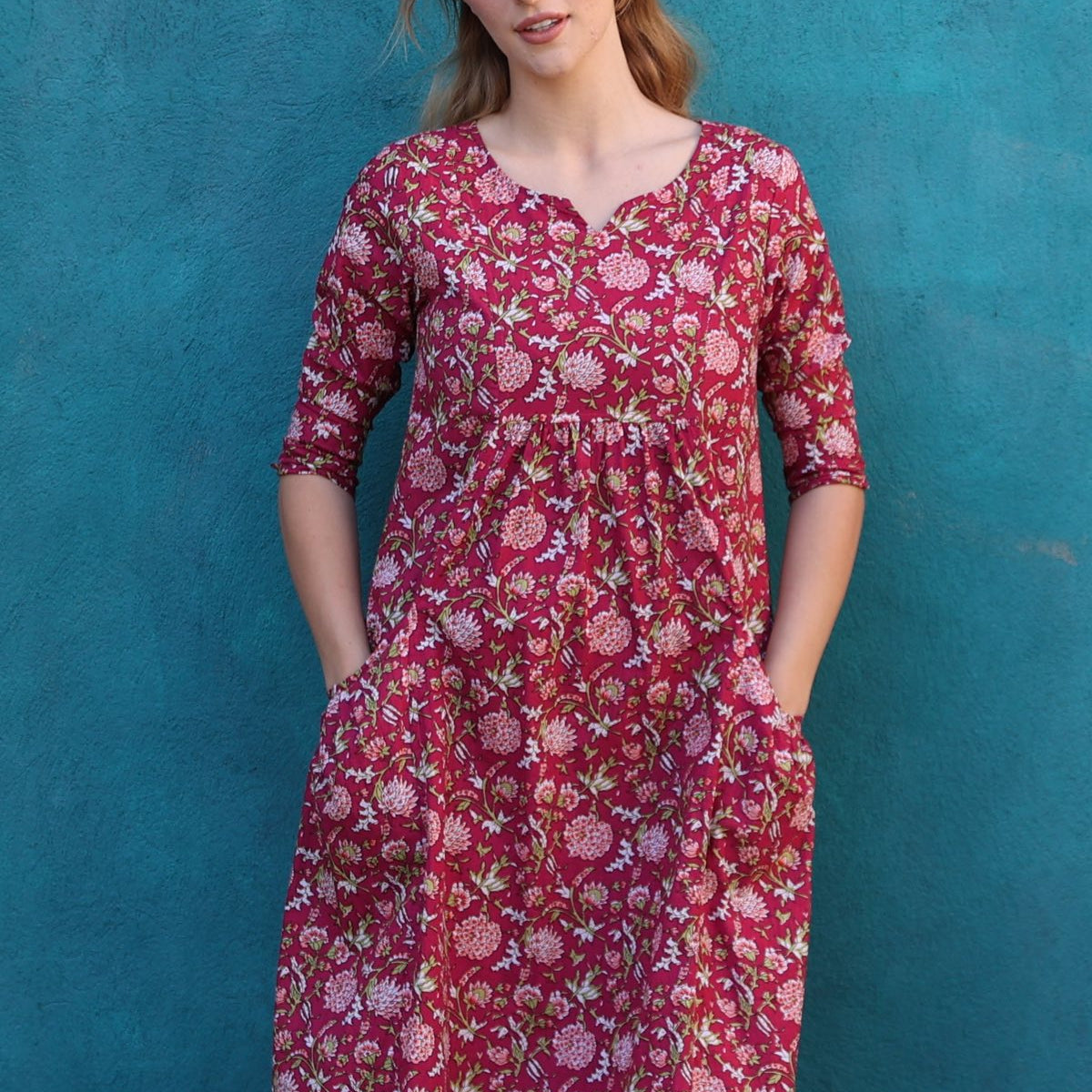 Model wearing 100%  cotton dress with beautiful floral print in pink, green and white on bright red base.