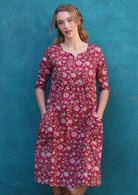 Model wearing 100%  cotton dress with beautiful floral print in pink, green and white on bright red base.