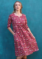 Model standing in front of blue wall wears  3/4 sleeves cotton dress with round neckline, pockets and pin tucks on waist.