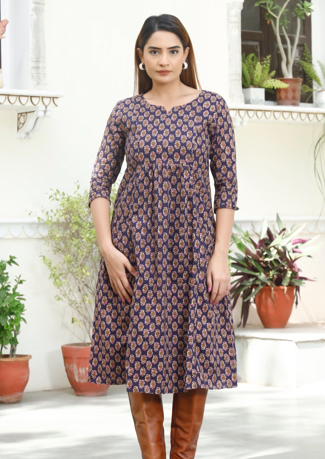 Model standing in 3/4 sleeved cotton dress with pockets, empire waist and round neckline.
