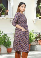 Side pose of model in gorgeous purple floral printed, knee length cotton dress with pockets.