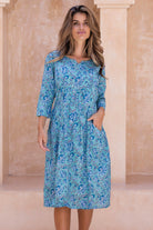 Woman wearing a aqua blue floral cotton dress with sleeves , hand in pocket