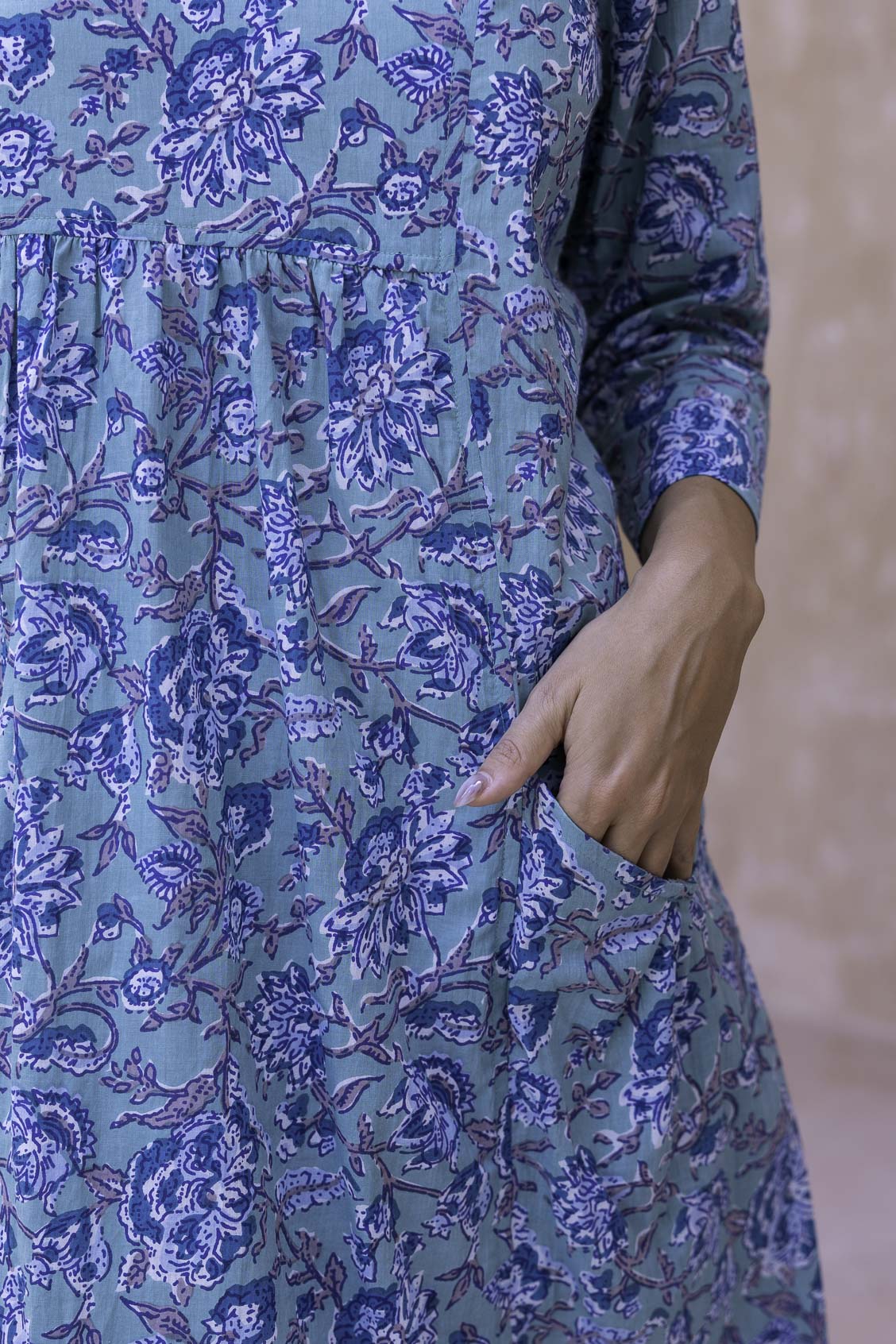 Woman wearing a aqua blue floral cotton dress with sleeves hand in pocket