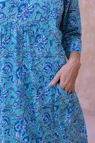 Woman wearing a aqua blue floral cotton dress with sleeves hand in pocket