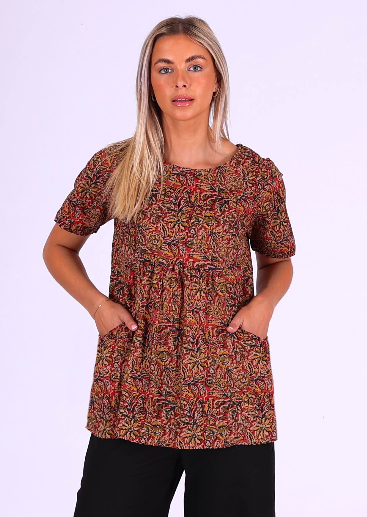 woman with blond hair wearing long cotton top Indian print in earthy tones with hands in pockets