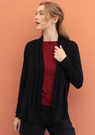 Woman wears black soft, stretch rayon cardi with long sleeves, holding the front opening revealing maroon top underneath