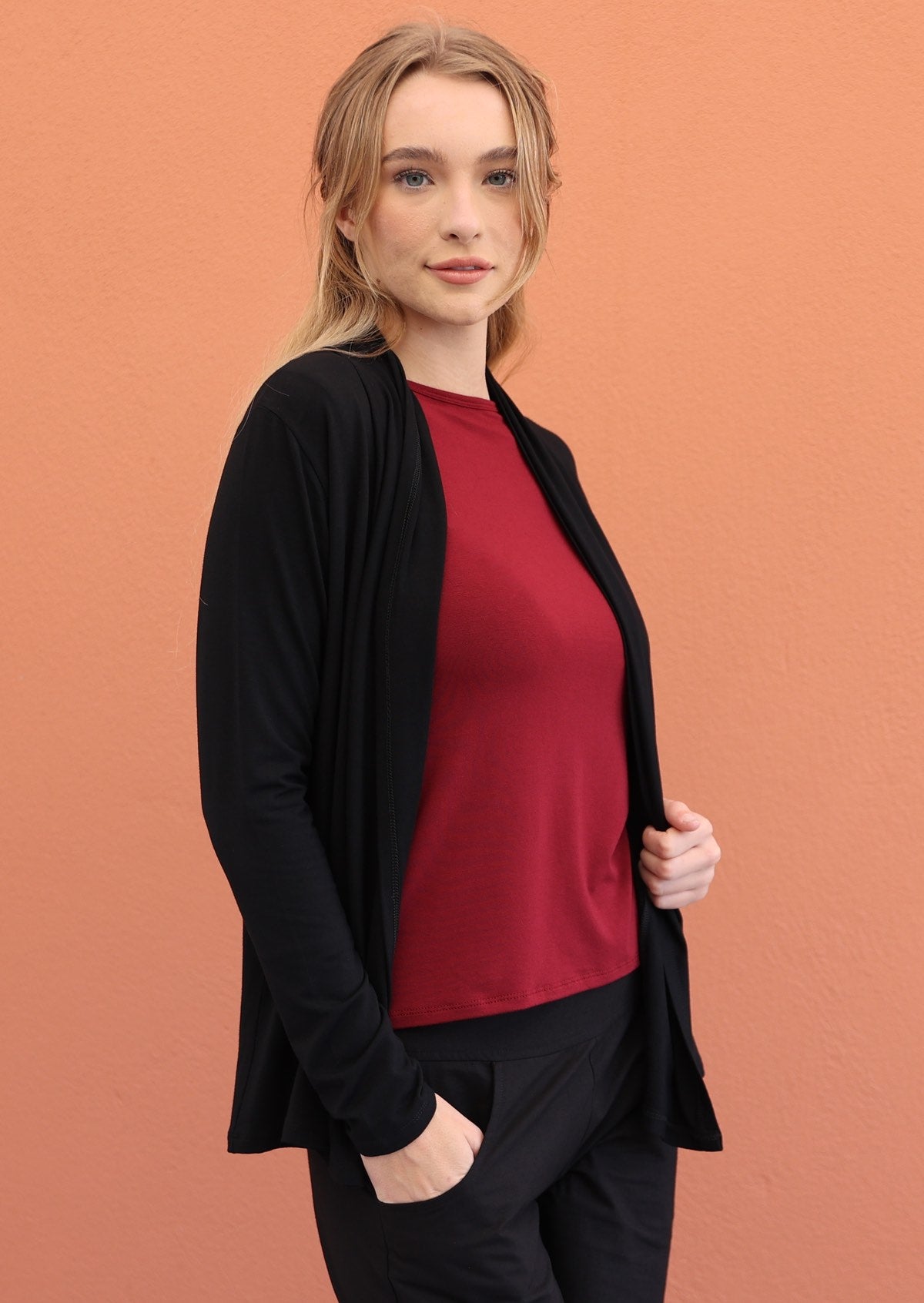 Model wears black soft, stretch rayon cardi with long sleeves, with hand in pocket of pants