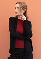 Model poses in black soft, stretch rayon cardi with long sleeves, open at front to reveal a maroon top underneath