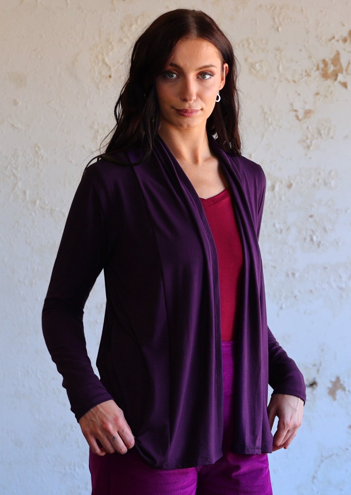 Model wearing dark purple soft, stretch rayon cardi with long sleeves, open at front revealing V neck maroon top underneath.