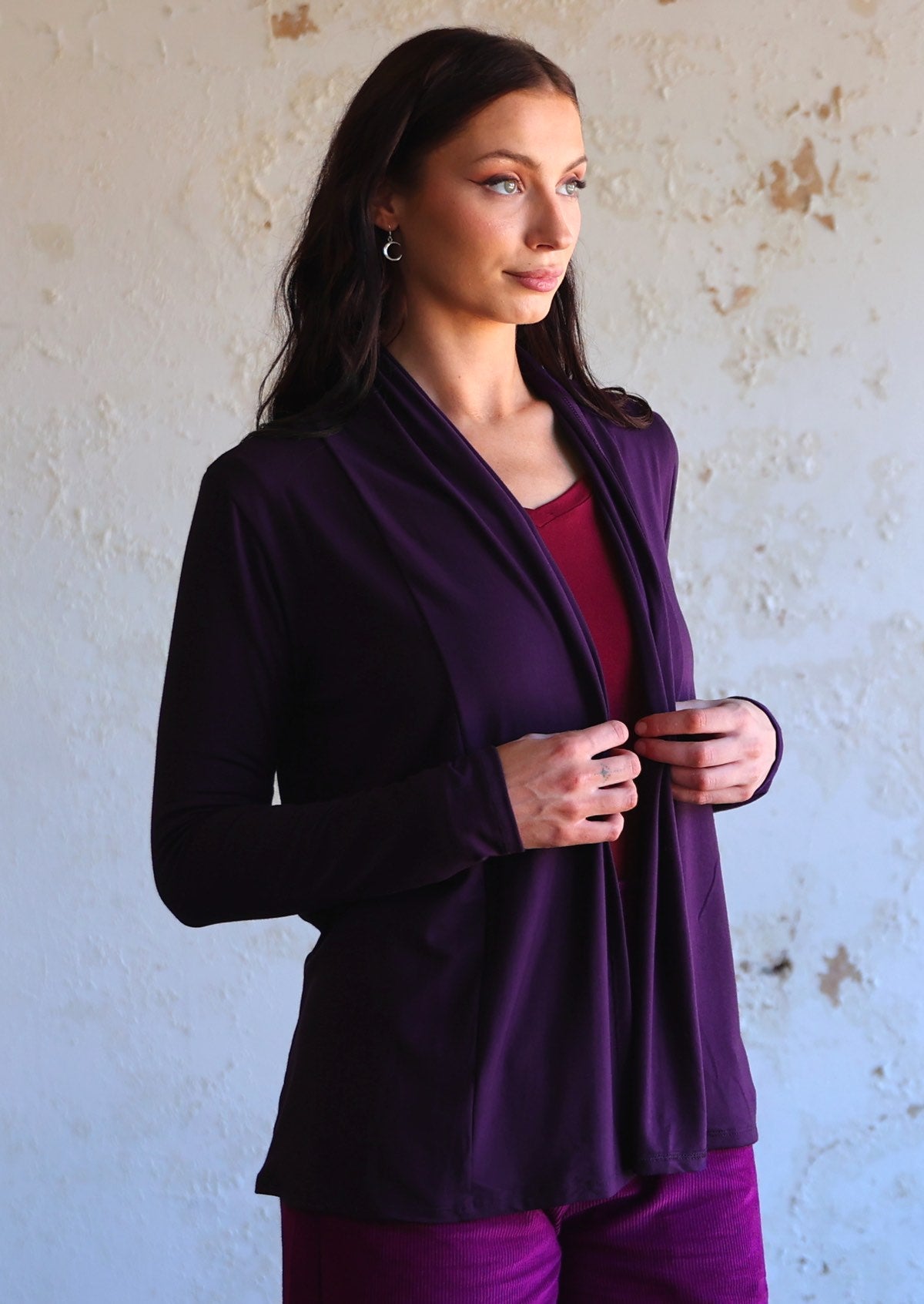 Model stands in dark purple soft, stretch rayon cardi with long sleeves, holding the hem in front.