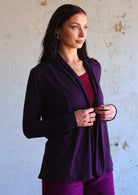 Model stands in dark purple soft, stretch rayon cardi with long sleeves, holding the hem in front.