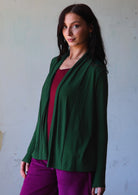 Model stands slightly sideways wearing a soft stretch rayon jersey in dark green with long sleeves and open front.