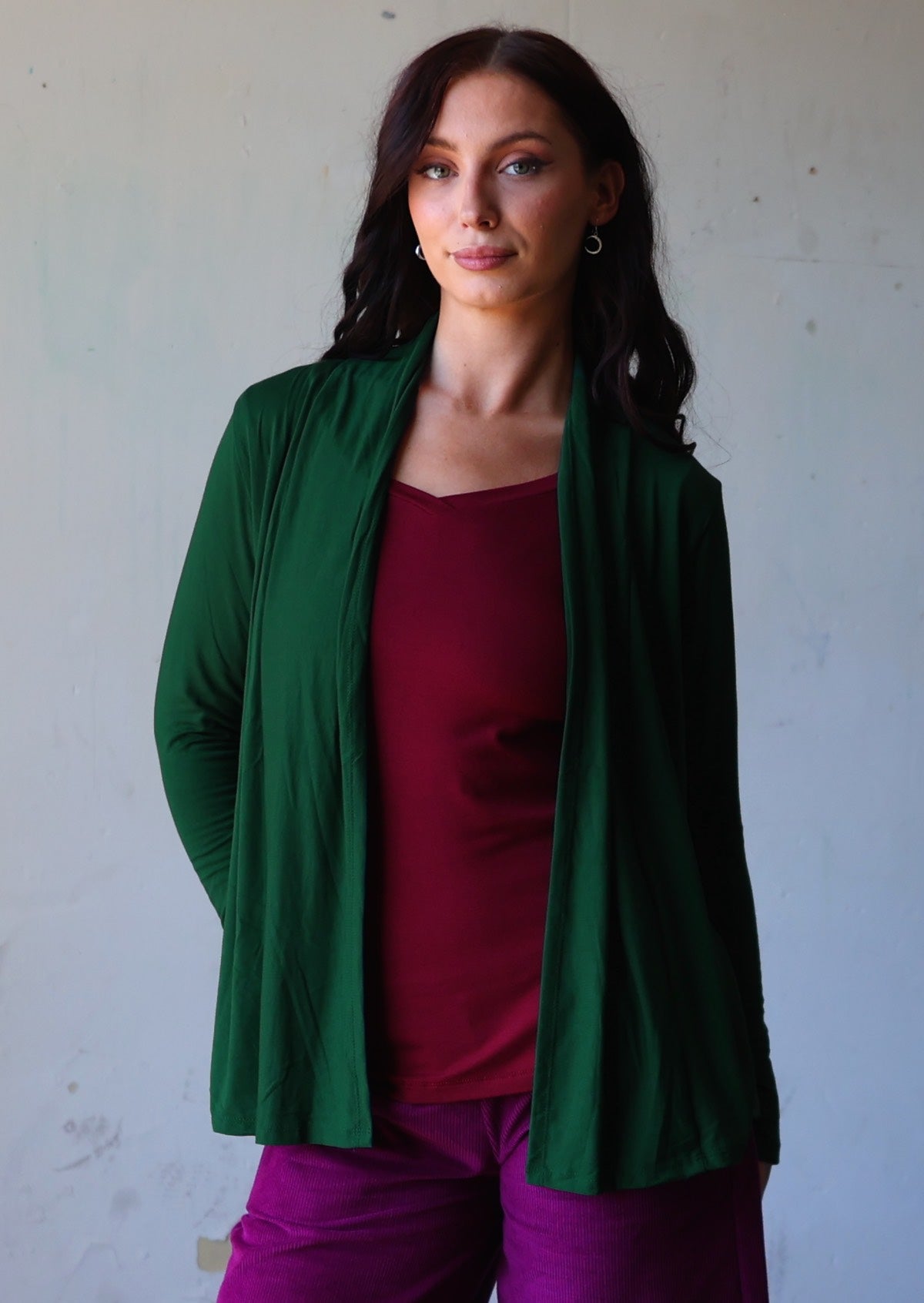 Model posing in dark green soft stretch cardigan with long sleeves and open front revealing maroon top.
