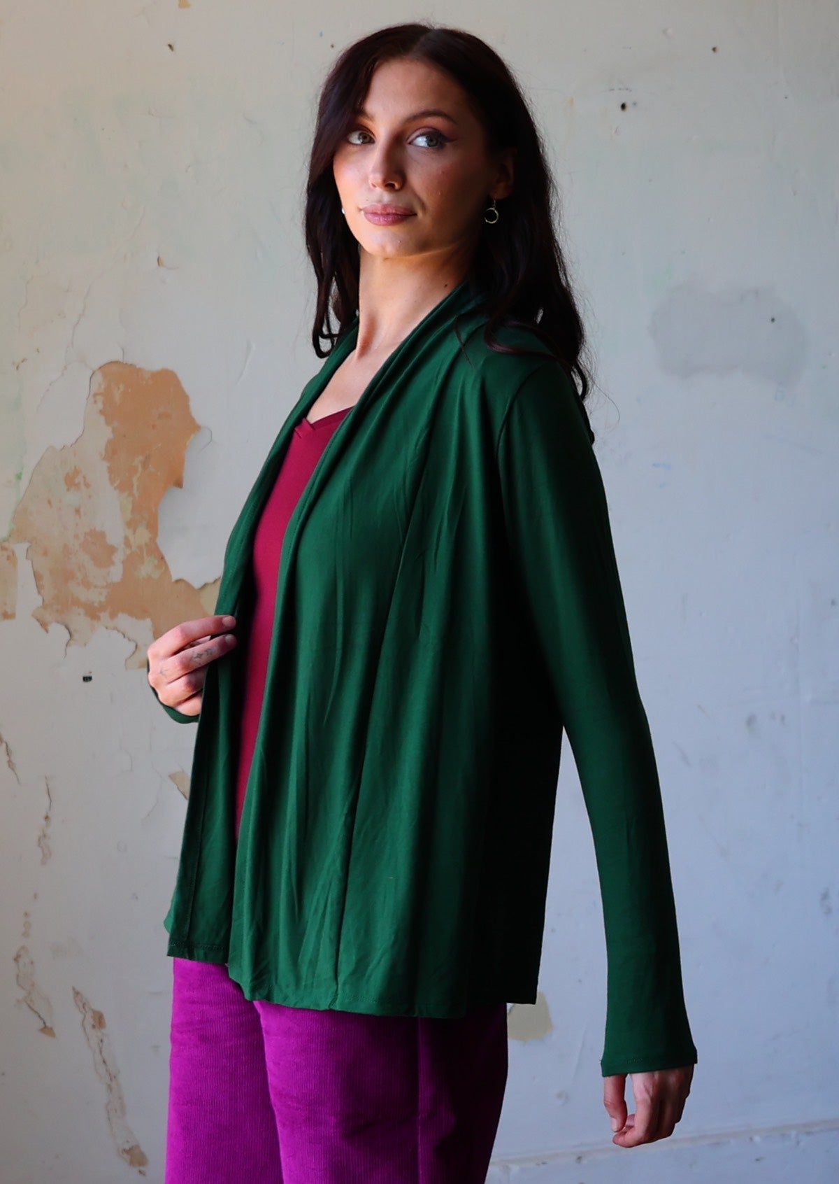 Woman wears dark green soft, stretch rayon cardi with long sleeves, holding the front opening revealing maroon top underneath.