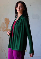 Woman wears dark green soft, stretch rayon cardi with long sleeves, holding the front opening revealing maroon top underneath.