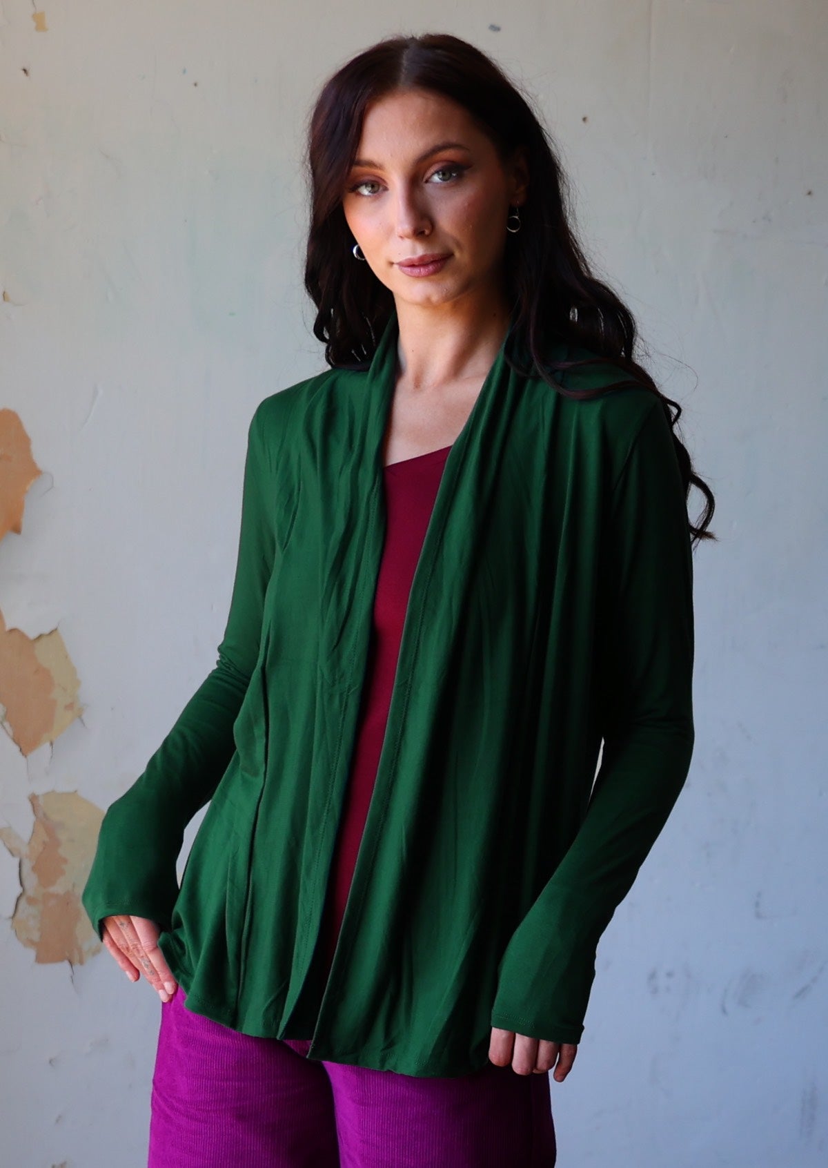 Model wears dark green soft, stretch rayon cardi with long sleeves, open at front to reveal a maroon top underneath