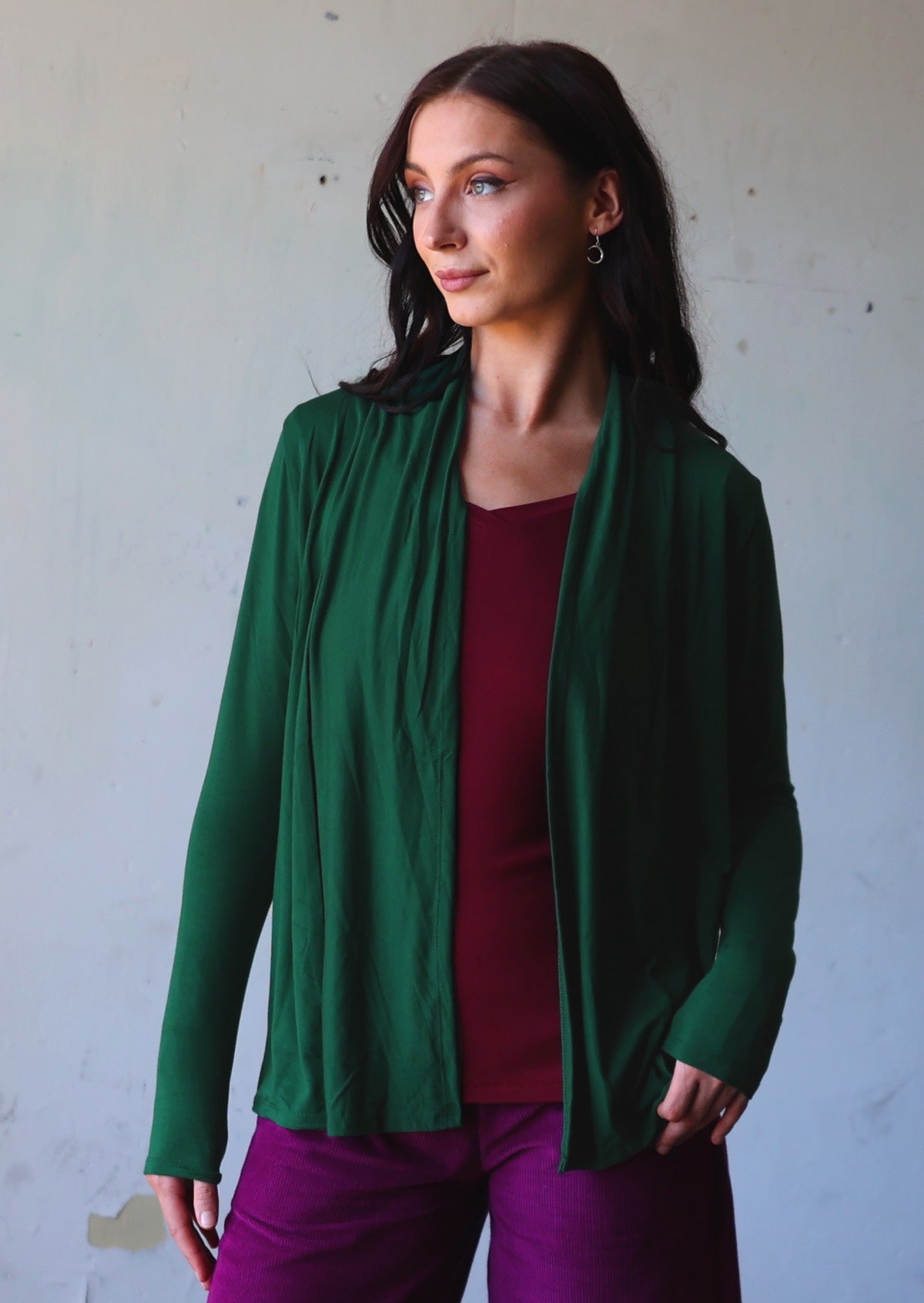 Woman poses in green soft, stretch rayon cardi with long sleeves and open neck.