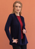 Woman wears navy blue soft, stretch rayon cardi with long sleeves, holding the front opening revealing maroon top underneath.