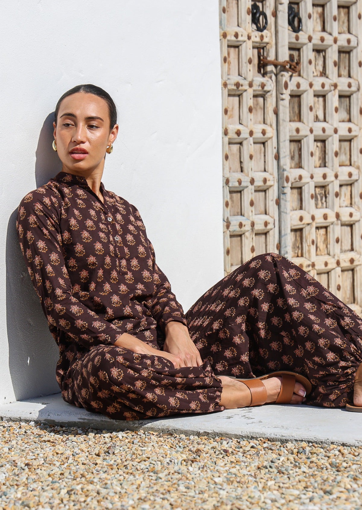 Woman sits in long sleeve cotton tunic with matching print harem pants, both with red floral motif print.