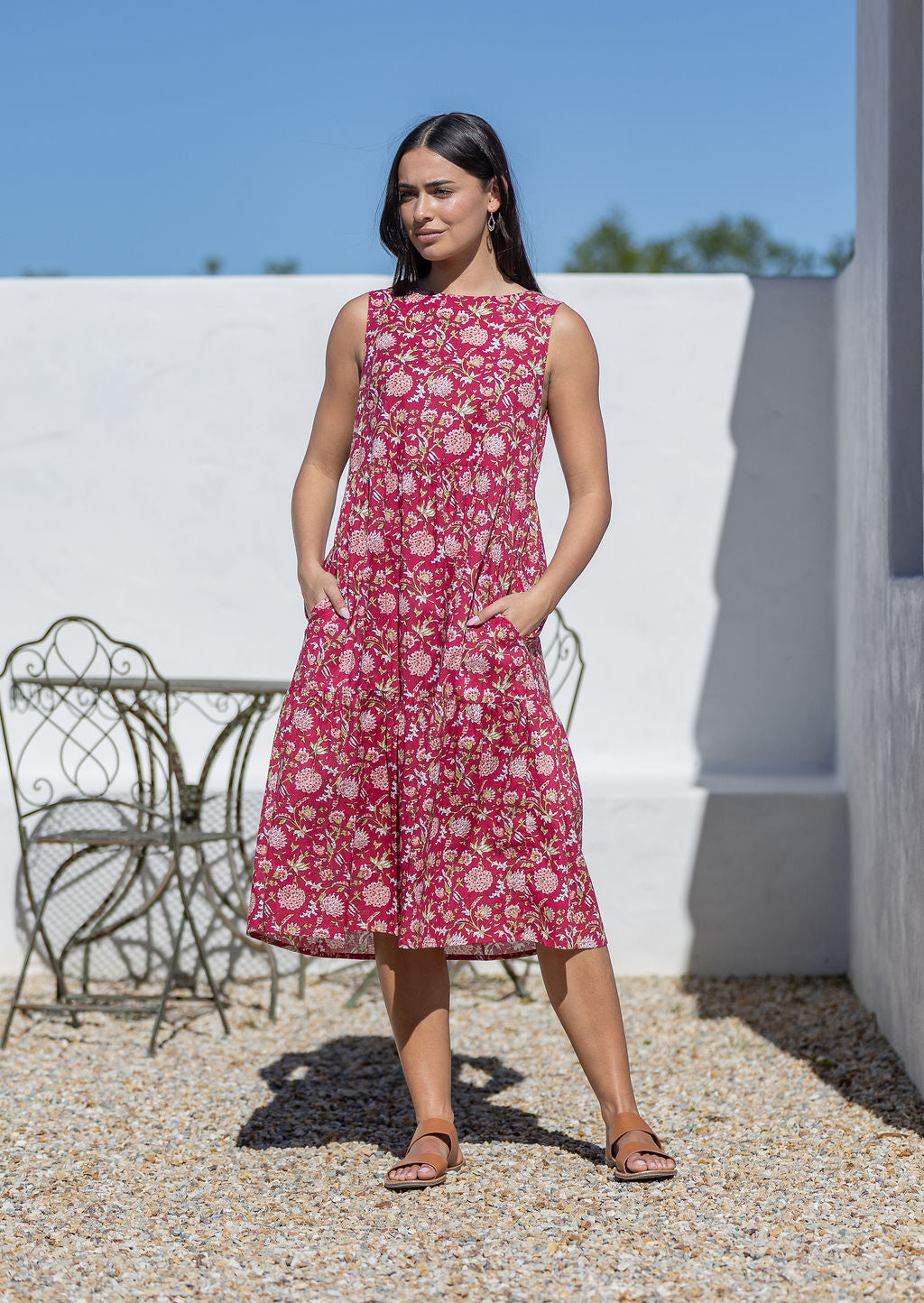 Woman wearing a pink floral cotton dress standing outdoors with a white wall with hands in pockets