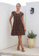 Women wears 100% cotton dress with pleated bodice, round neckline and short caped sleeves.