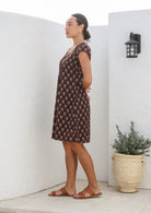 Side pose of model wearing 100% cotton mini dress with short cap sleeves, pleated bodice and round neckline.