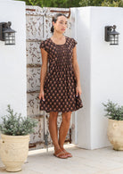 Model is wearing a knee length cotton dress in dark brown based floral print.